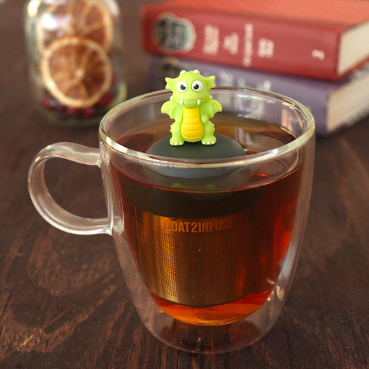 bright green dragon tea infuser for loose leaf tea  with a fine mesh stainless steel tea infuser that reads FLOAT2INFUSE on a black base floating in a glass tea mug with books in the background