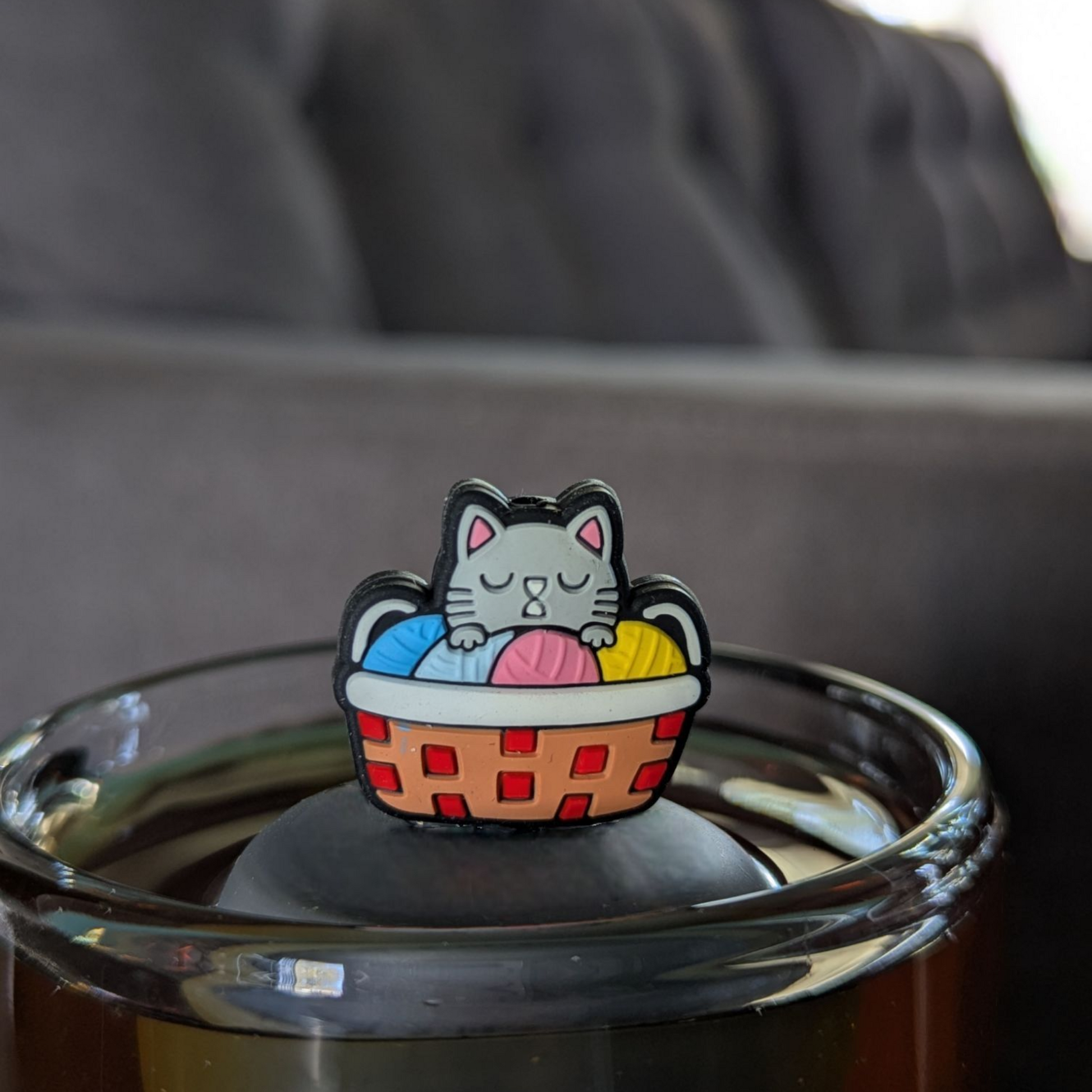 grey cat in colorful knitting basket animal  tea infuser for Loose leaf tea with a fine mesh stainless steel Tea steeper that reads FLOAT2INFUSE on black base floating in a Glass tea mug with a couch in the background