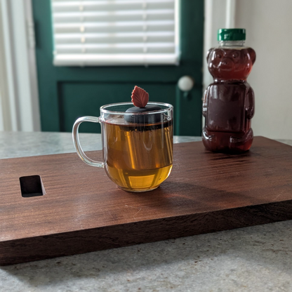 maroon leaf tea infuser for loose leaf tea  with a fine mesh stainless steel tea infuser that reads FLOAT2INFUSE on a black base floating in a glass tea mug with a honey bear in the background