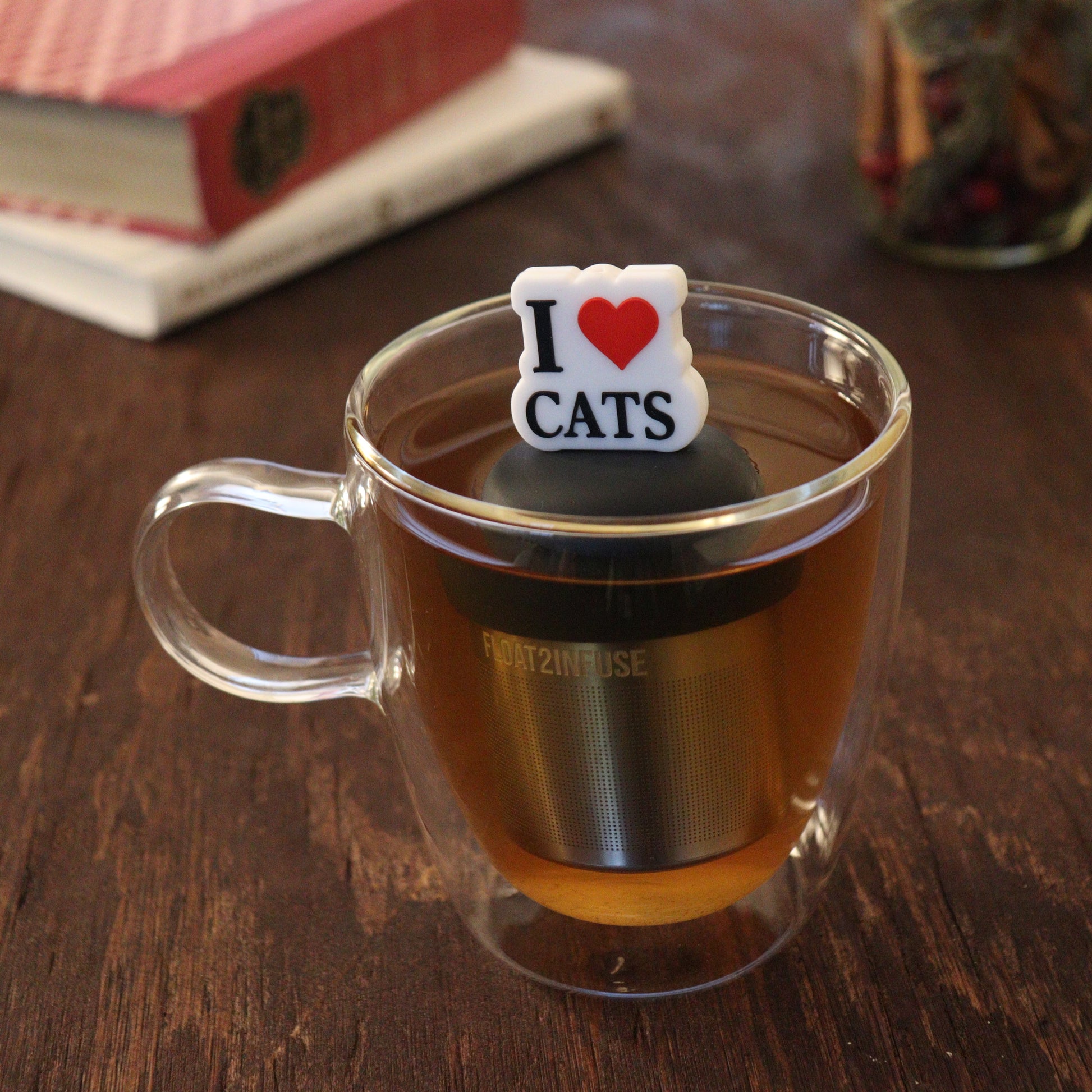 black text on white background that reads "i love cats" with red heart tea infuser for loose leaf tea on a black base with a fine mesh stainless steel tea infuser that reads FLOAT2INFUSE floating in a glass tea mug with books and loose leaf tea in the background