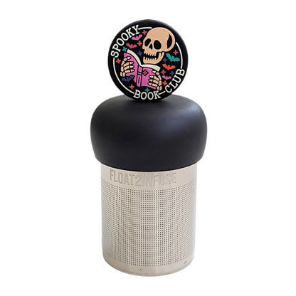 Black circle with an ivory skeleton reading a pink book with the text "spooky book club" and multicolored bats circling it tea infuser for loose leaf tea with a fine mesh stainless steel tea strainer that reads FLOAT2INFUSE on a black base with a white background