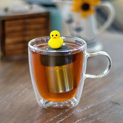 yellow rubber duck tea infuser for loose leaf tea with a fine mesh stainless steel tea strainer that reads FLOAT2INFUSE on a black base  floating in a glass tea mug with a drink pitcher in the background