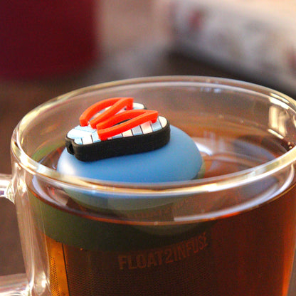 Americana blue and white striped flip flops with red straps tea infuser for loose leaf tea with a fine mesh stainless steel tea strainer that reads FLOAT2INFUSE on a blue base  floating in a glass tea mug 
with books in the background
