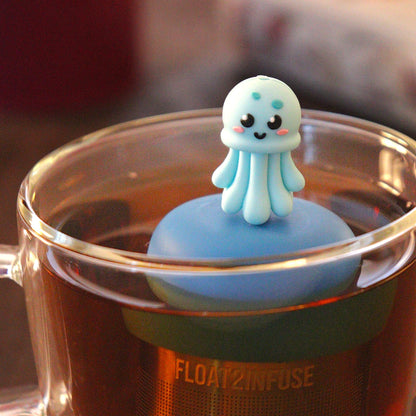 blue jellyfish animal tea infuser for loose leaf tea  with a fine mesh stainless steel tea strainer that reads FLOAT2INFUSE on a blue base floating in a glass tea mug