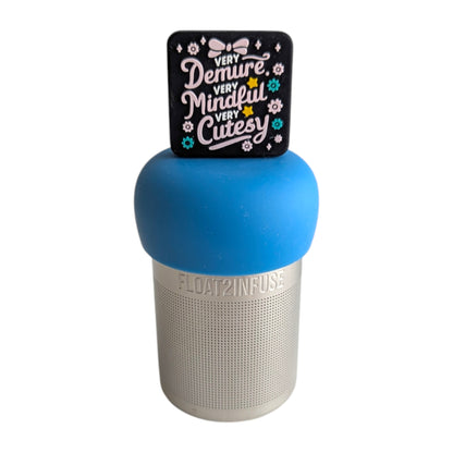 Black square with pink text that reads "very demure, very mindful, very cutesy" with pink and teal flowers and a pink bow tea infuser for loose leaf tea with a fine mesh stainless steel tea strainer that reads FLOAT2INFUSE on a blue base with a white background