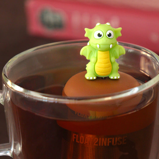 bright green dragon tea infuser for loose leaf tea  with a fine mesh stainless steel tea strainer that reads FLOAT2INFUSE on a brown base floating in a glass tea mug with books in the background