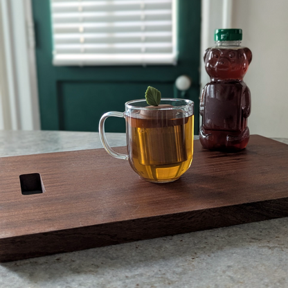 green herb leaf tea infuser for loose leaf tea with fine mesh stainless steel tea strainer that reads FLOAT2INFUSE on a brown base floating in a glass tea mug with a honey bear in the background