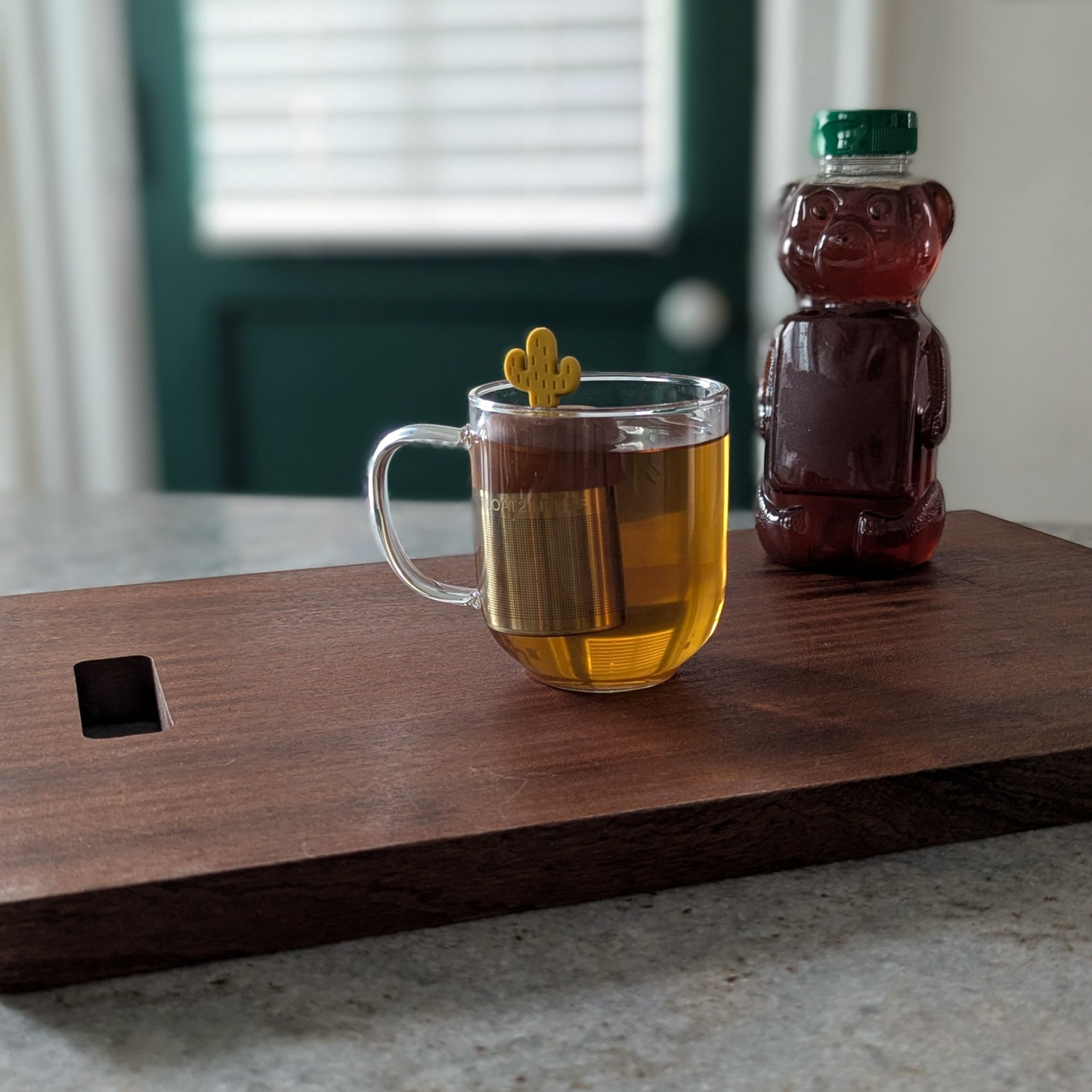 yellow cactus tea infuser for loose leaf tea  with a fine mesh stainless steel tea steeper that reads FLOAT2INFUSE on a brown base floating in a glass tea mug with a honey bear in the background