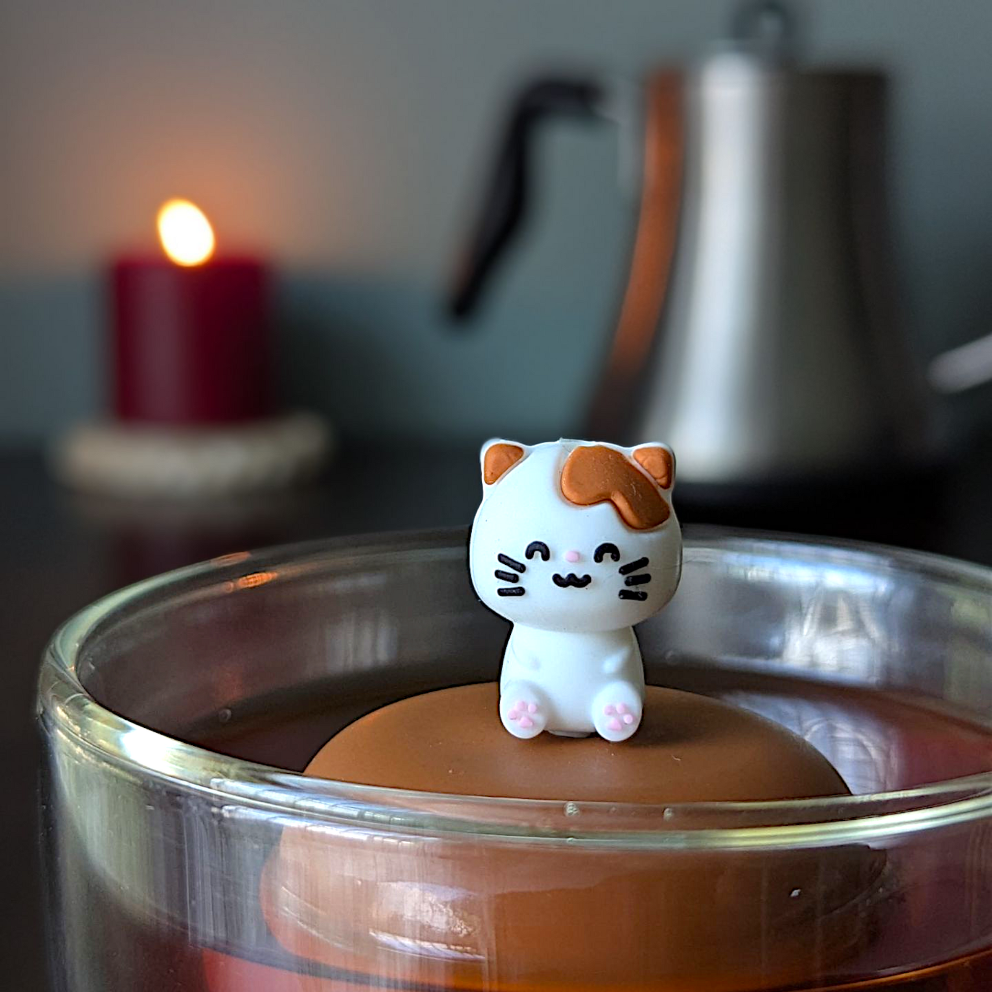 white brown kitty cat floating tea infuser ina glass cup with a blurred background