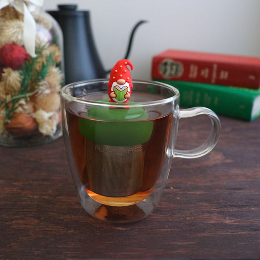 red holiday candy with green, yellow, and white polka dots tea infuser for loose leaf tea with a fine mesh stainless steel tea strainer that reads FLOAT2INFUSE on a dark green base with books, a tea kettle, and christmas decorations in the background