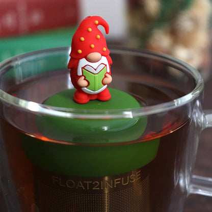 red holiday candy with green, yellow, and white polka dots tea infuser for loose leaf tea with a fine mesh stainless steel tea strainer that reads FLOAT2INFUSE on a dark green base with books, a tea kettle, and christmas decorations in the background