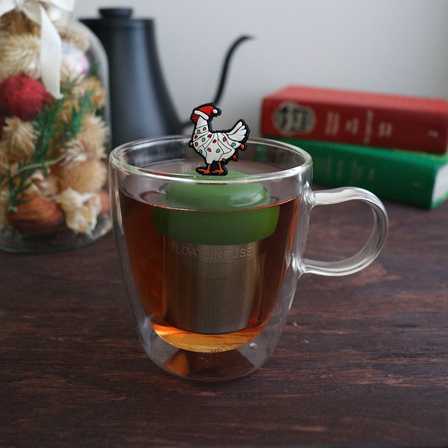 White chicken wearing a santa hat and wrapped in red and green christmas lights  tea infuser for loose leaf tea with a fine mesh stainless steel tea strainer  that reads FLOAT2INFUSE on a dark green base with a white background