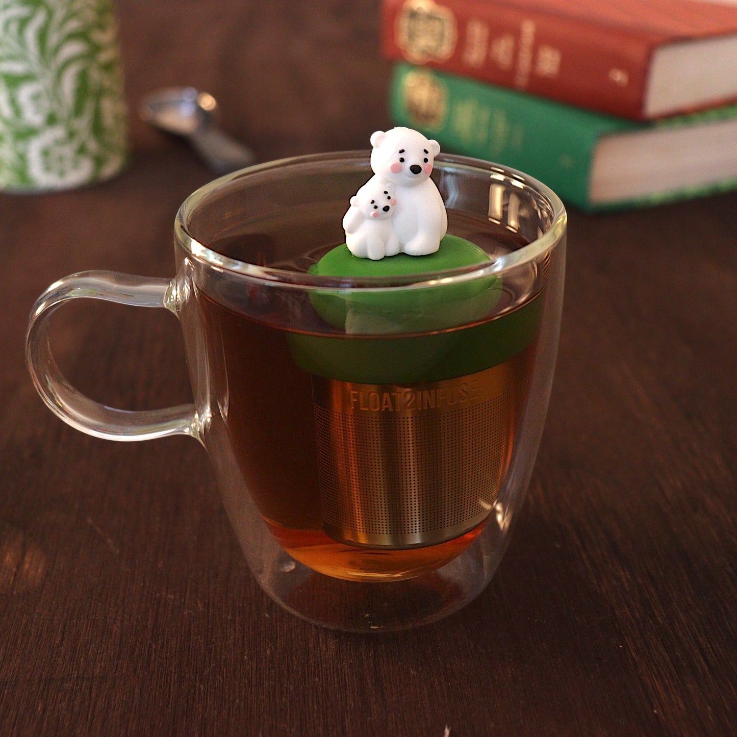 cute mom and baby polar bear tea infuser for loose leaf tea with a fine mesh stainless steel tea strainer 
that reads FLOAT2INFUSE on a dark green base with a tea canister and books in the background