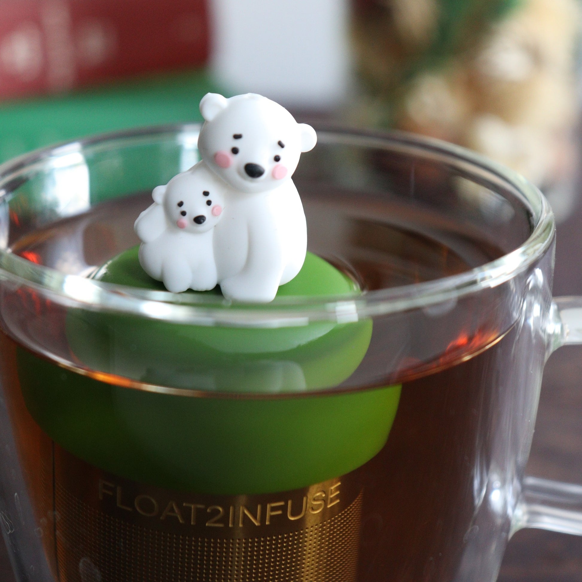 cute mom and baby polar bear tea infuser for loose leaf tea with a fine mesh stainless steel tea strainer 
that reads FLOAT2INFUSE on a dark green base with a tea canister and books in the background