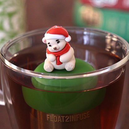 Cozy white polar bear wearing a red and white santa hat and a red scarf tea infuser for loose leaf tea with a fine mesh stainless steel tea strainer 
that reads FLOAT2INFUSE on a dark green base with books and a tea canister in the background