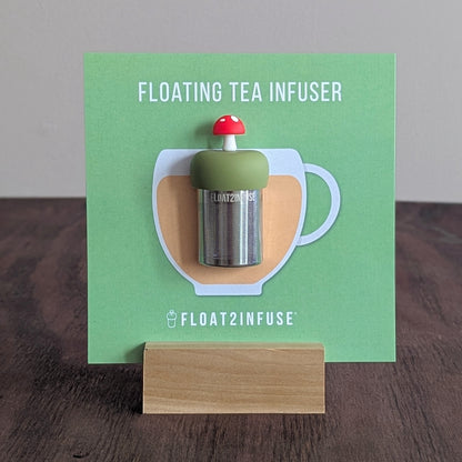 Floating red mushroom tea infuser on a green card with 'FLOAT2INFUSE' branding