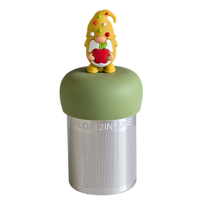 gnome with long white beard wearing yellow with red, white and green polka dots on the hat and holding a red apple animal tea infuser for loose leaf tea with a fine mesh stainless steel tea strainer that reads FLOAT2INFUSE on a green base with a white background