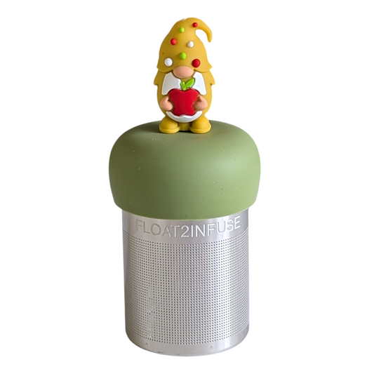 gnome with long white beard wearing yellow with red, white and green polka dots on the hat and holding a red apple animal tea infuser for loose leaf tea with a fine mesh stainless steel tea strainer that reads FLOAT2INFUSE on a green base with a white background