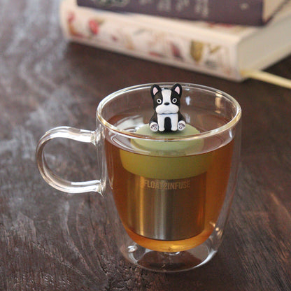 black and white terrier dog animal tea infuser for loose leaf tea on a green base with a fine mesh stainless steel tea infuser that reads FLOAT2INFUSE floating in a glass tea mug with books in the background