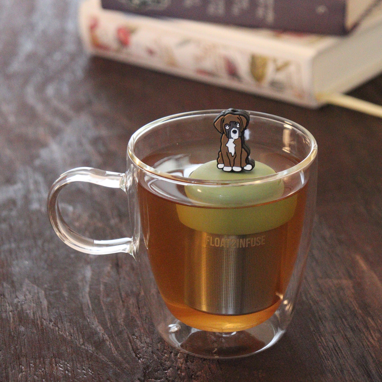 brown boxer dog animal tea infuser for loose leaf tea on a green base with a fine mesh stainless steel tea infuser that reads FLOAT2INFUSE floating in a glass tea mug with books in the background