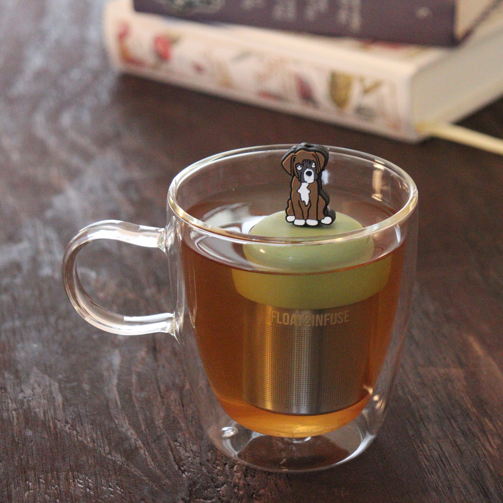 brown boxer dog animal tea infuser for loose leaf tea on a green base with a fine mesh stainless steel tea infuser that reads FLOAT2INFUSE floating in a glass tea mug with books in the background