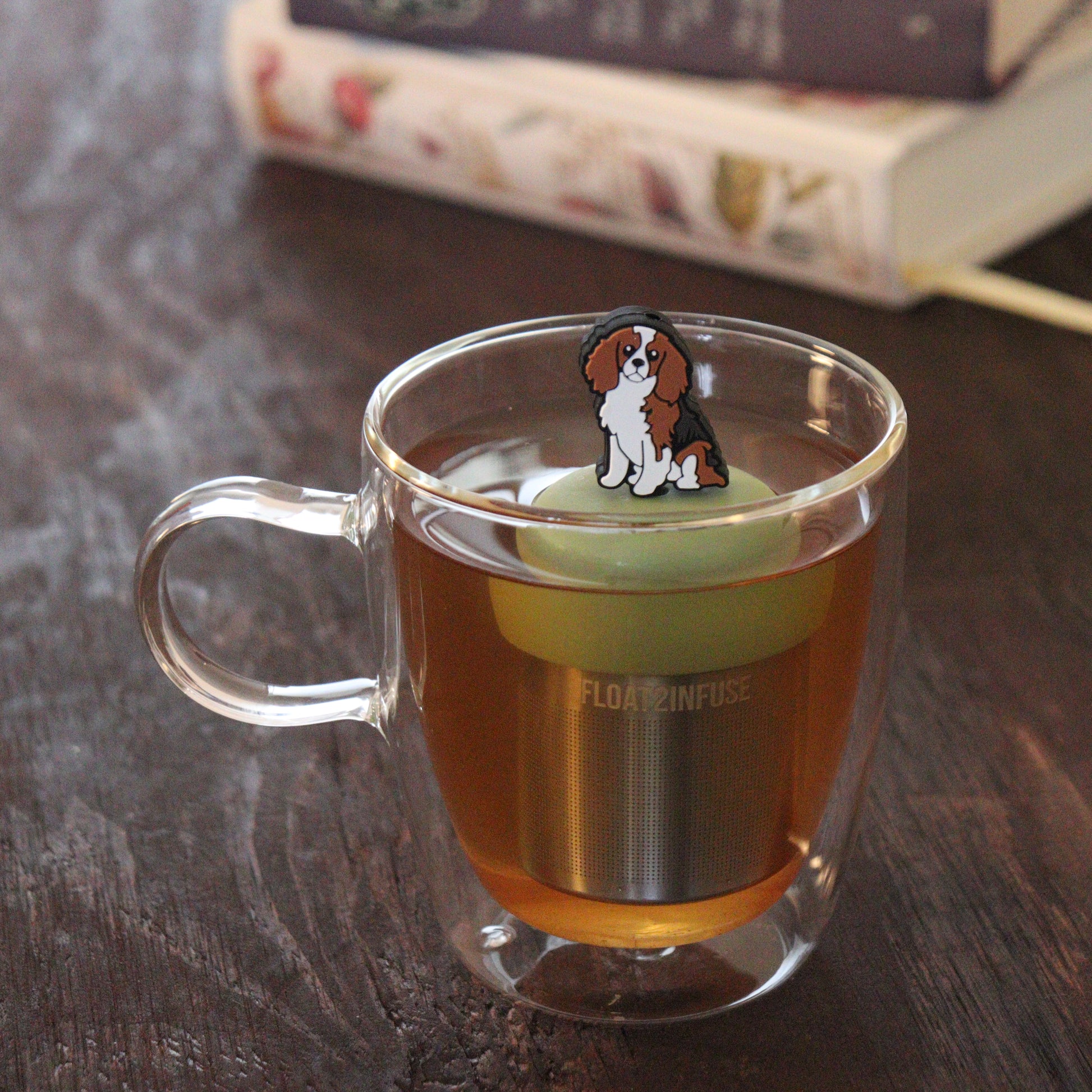 brown and white cocker spaniel dog animal tea infuser for loose leaf tea on a green base with a fine mesh stainless steel tea infuser that reads FLOAT2INFUSE floating in a glass tea mug with books in the background