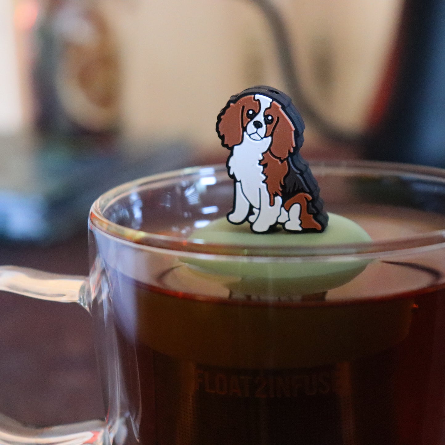 cocker spaniel dog animal tea infuser for loose leaf tea on a green base with a fine mesh stainless steel tea strainer that reads FLOAT2INFUSE floating in a glass tea mug with tea kettle in the background