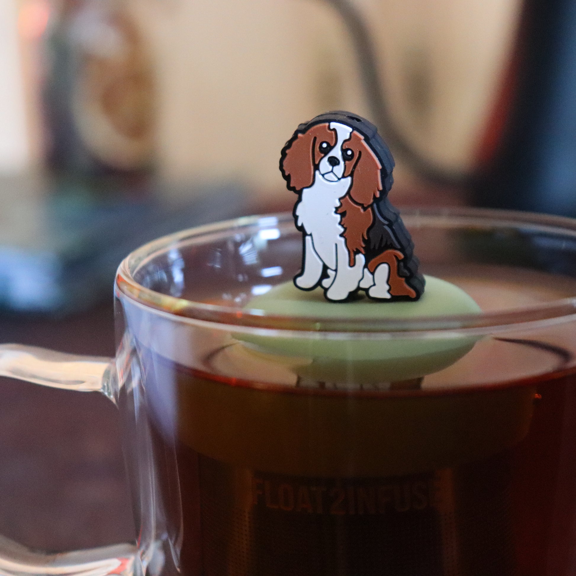 cocker spaniel dog animal tea infuser for loose leaf tea on a green base with a fine mesh stainless steel tea strainer that reads FLOAT2INFUSE floating in a glass tea mug with tea kettle in the background