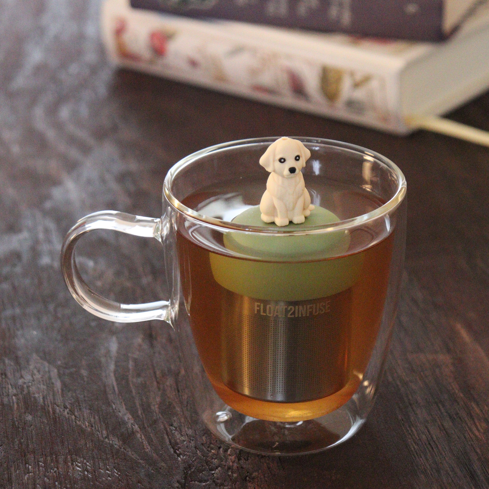 golden retriever dog animal tea infuser for loose leaf tea  with a fine mesh stainless steel tea infuser that reads FLOAT2INFUSE on a green base floating in a glass tea mug with books in the background