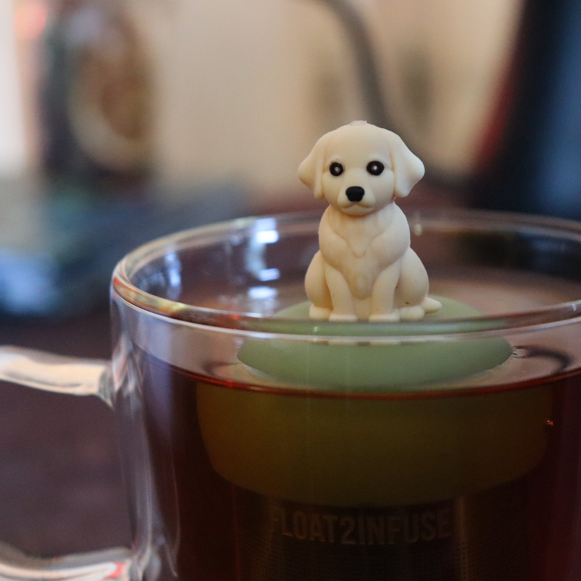 golden retriever dog animal tea infuser for loose leaf tea  with a fine mesh stainless steel tea strainer that reads FLOAT2INFUSE on a green base floating in a glass tea mug with tea kettle in the background