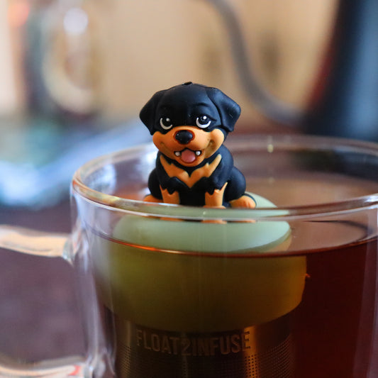 black and brown rottweiler dog animal tea infuser for loose leaf tea on a green base with a fine mesh stainless steel tea strainer that reads FLOAT2INFUSE floating in a glass tea mug with tea kettle in the background