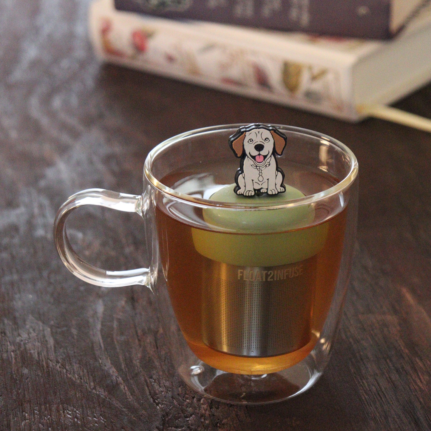 yellow Labrador Retriever dog animal tea infuser for loose leaf tea  with a fine mesh stainless steel tea infuser that reads FLOAT2INFUSE on a green base floating in a glass tea mug with books in the background