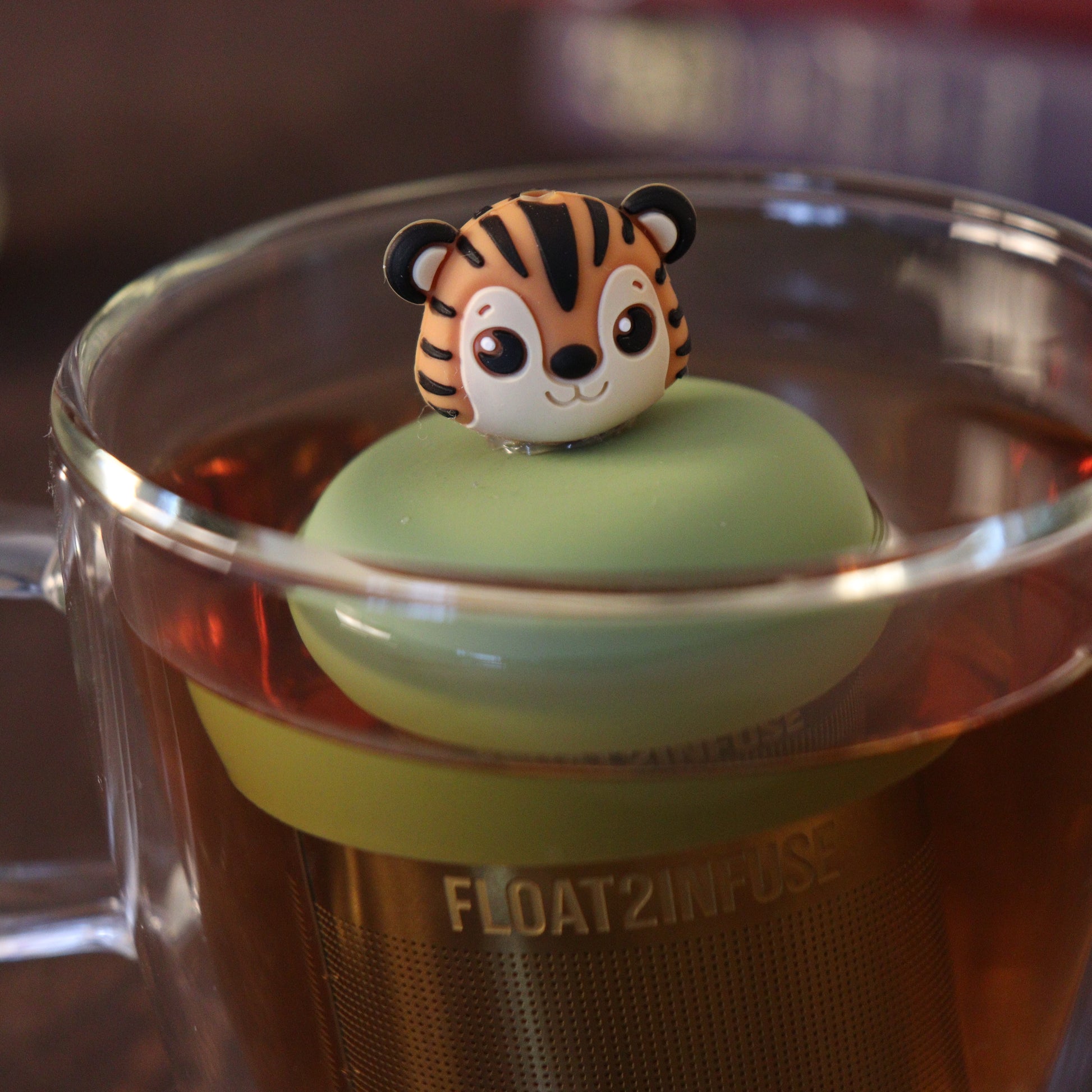 tiger tea infuser with a fine mesh stainless steel tea strainer that says FLOAT2INFUSE in a glass tea mug