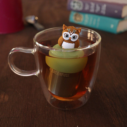 Cute boho brown owl infuser for loose leaf tea with a fine mesh stainless steel tea strainer 
that reads FLOAT2INFUSE on a green base with a tea canister and books in the background
