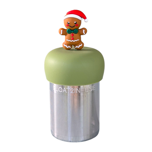 Smiling gingerbread man wearing a red santa hat and a green bowtie tea infuser for loose leaf tea with a fine mesh stainless steel tea strainer that reads FLOAT2INFUSE on a green base  with a white background