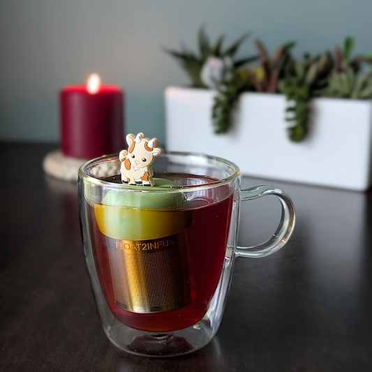 Brown and beige goat tea infuser for loose leaf tea with a fine mesh stainless steel tea strainer that reads FLOAT2INFUSE on a green base  with plants and plants in the background