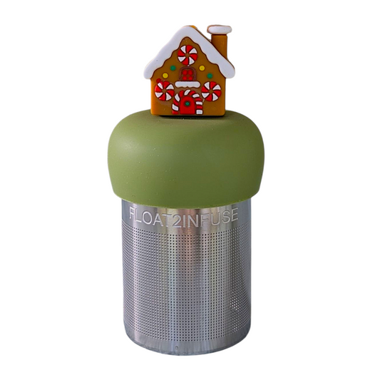 Brown gingerbread house with peppermint candy windows and snow on the roof tea infuser for loose leaf tea with a fine mesh stainless steel tea strainer that reads FLOAT2INFUSE on a green base with a white background