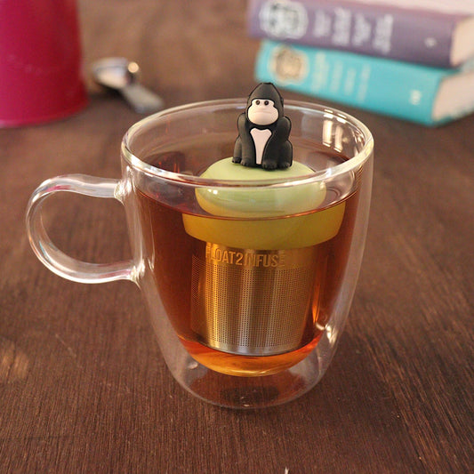 Black gorilla tea infuser for loose leaf tea with a fine mesh stainless steel tea strainer that reads FLOAT2INFUSE on a green base with a tea canister and books in the background