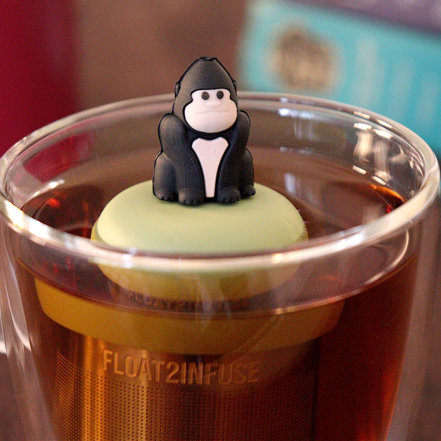 Black gorilla tea infuser for loose leaf tea with a fine mesh stainless steel tea strainer that reads FLOAT2INFUSE on a green base with a tea canister and books in the background