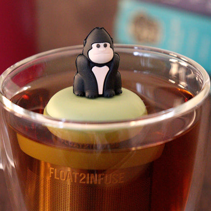 Black gorilla tea infuser for loose leaf tea with a fine mesh stainless steel tea strainer that reads FLOAT2INFUSE on a green base with a tea canister and books in the background