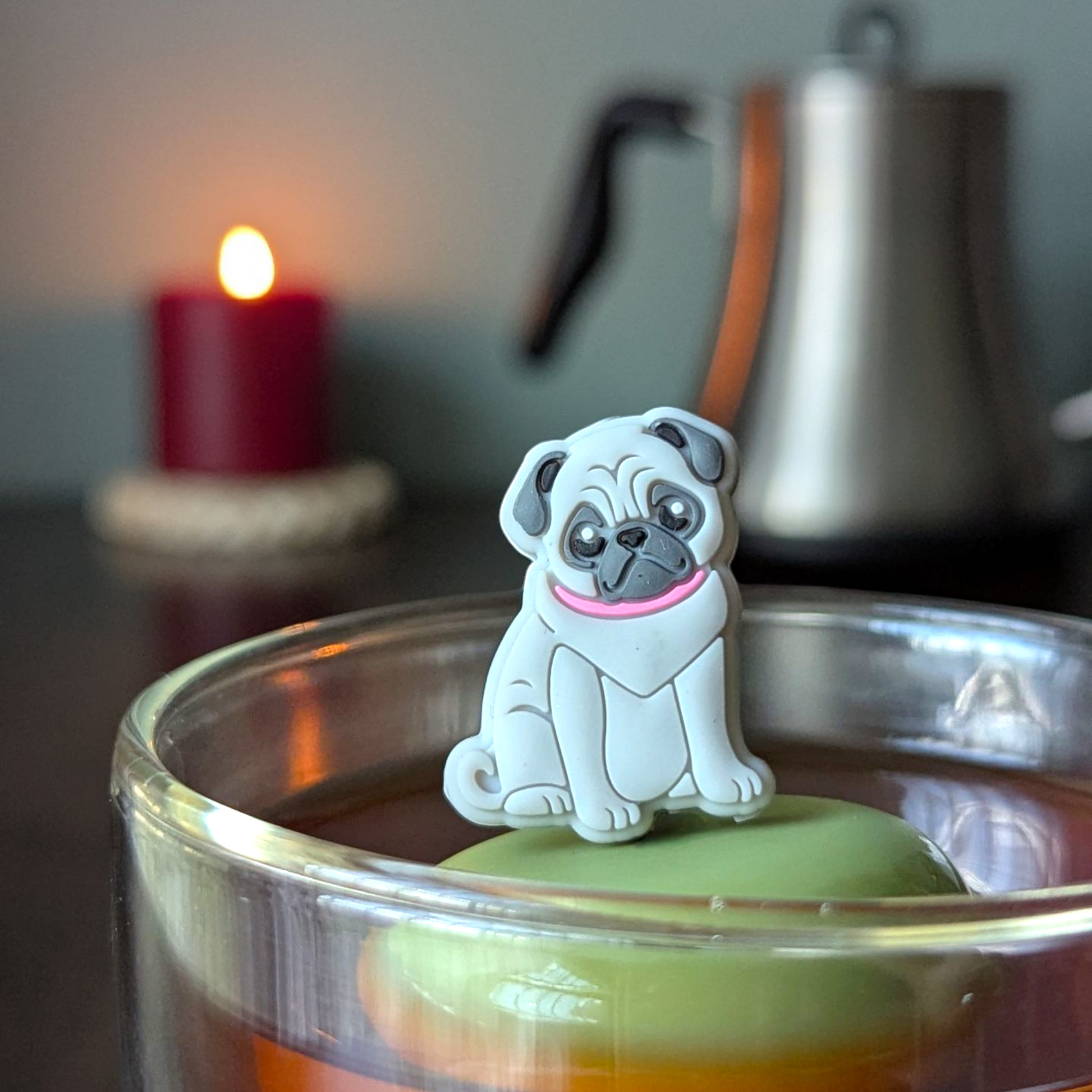 grey pug dog tea infuser for loose leaf tea with a fine mesh stainless steel tea strainer that reads FLOAT2INFUSE on a green base  with  a lit candle and a tea kettle in the background