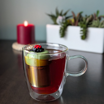 red and black ladybug tea infuser for loose leaf tea with a fine mesh stainless steel tea strainer that reads FLOAT2INFUSE on a green base with a lit candle and plants in the background
