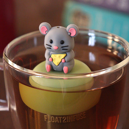 adorable grey mouse with yellow cheese wedge tea infuser for loose leaf tea with a fine mesh stainless steel tea strainer 
that reads FLOAT2INFUSE on a green base with a tea canister and books in the background