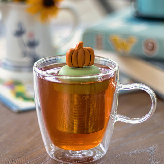 orange pumpkin tea infuser for loose leaf tea with a fine mesh stainless steel tea strainer that reads FLOAT2INFUSE on a green base  floating in a glass tea mug 
with books in the background