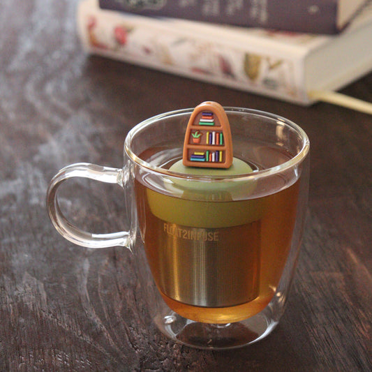plant bookshelf tea infuser for loose leaf tea with a fine mesh stainless steel tea infuser that reads FLOAT2INFUSE on a green base floating in a glass tea mug with books in the background