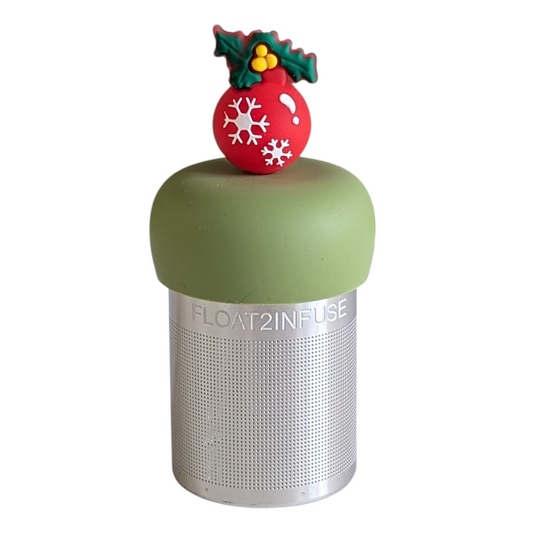 red ball christmas ornament with white snowflakes and green holly plant tea infuser for loose leaf tea with a fine mesh stainless steel tea strainer that reads FLOAT2INFUSE on a green base with a white background