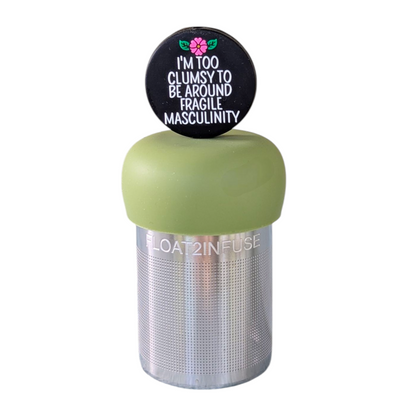 black circle with white text that reads "I'm too clumsy to be around fragile masculinity" with a pink  flower tea infuser  for loose leaf tea with fine mesh stainless steel tea strainer that reads FLOAT2INFUSE on a green base with a white background