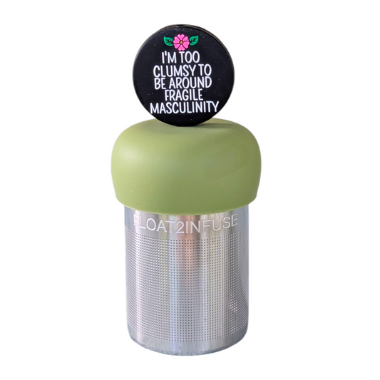 black circle with white text that reads "I'm too clumsy to be around fragile masculinity" with a pink  flower tea infuser  for loose leaf tea with fine mesh stainless steel tea strainer that reads FLOAT2INFUSE on a green base with a white background