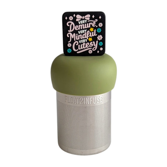 Black square with pink text that reads "very demure, very mindful, very cutesty" with pink and teal flowers and a pink bow tea infuser for loose leaf tea with a fine mesh stainless steel tea strainer that reads FLOAT2INFUSE on a green base with a white background
