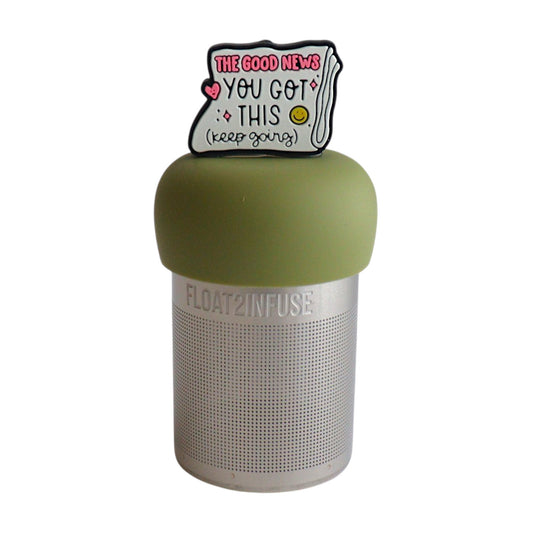 Folded newspaper with text that reads "The good news. You've got this. Keep going" with a pink heart and a yellow smiley face tea infuser for loose leaf tea  with a fine mesh stainless steel tea infuser that reads FLOAT2INFUSE on a green base with a white background